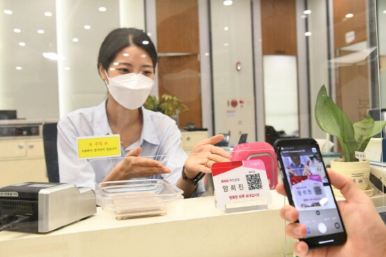 고객이 영업점 창구에서 디지털 실명확인을 위해 휴대폰 QR코드를 스캔 중인 장면.