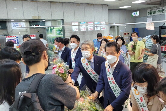 마산시농협 본점 하나로마트 내방 고객들에게 꽃을 나눠주는 박상진 마산시농협 조합장(중앙), 김주양 경남농협 본부장(좌측), 최성환 부경원예농협 조합장(우측). 사진=경남농협 제공